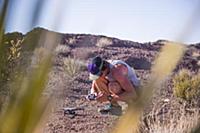 Man squatting in desert looking at control panel f