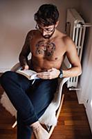 Mid adult man with tattooed chest sitting on chair