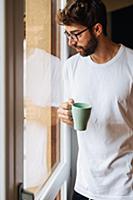 Mid adult man with coffee looking out through apar