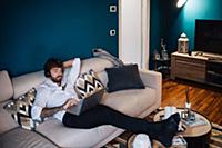 Mid adult man reclining on sofa listening to headp