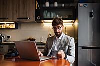 Mid adult man sitting at kitchen table with laptop