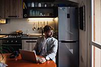 Mid adult man sitting at kitchen table with laptop