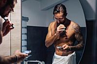 Mid adult man with tattoos brushing teeth and look
