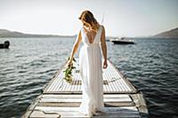 Young bride in wedding dress standing on lake pier