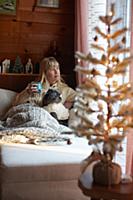 Woman drinking and cuddling dog on sofa at home