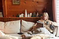 Woman reading book with dog on sofa at home