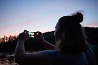 Woman taking photograph of sunset with smartphone