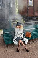 Blonde woman wearing trench coat and hat while sit