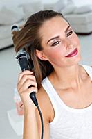 Beautiful brown eyed woman curling her hair with c