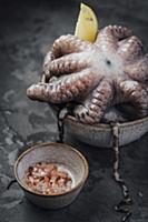 Fresh octopus in a bowl with lemon and pink salt