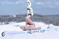 Young nude woman is laying with ski on snowpack wi